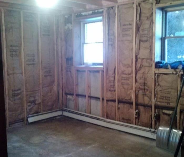 Image shows drywall and carpet removed from room with studs and concrete floor exposed.