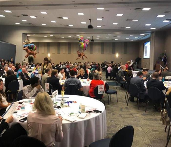 Image shows room of people at tables waiting for a presention to start.