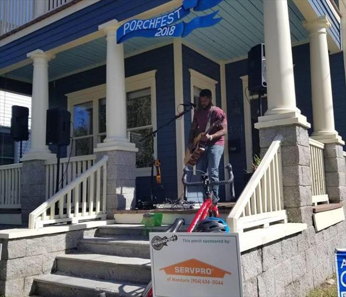 Image shows musician performing on the porch of someone's home.