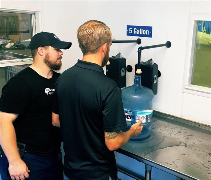 Image shows young men filling up 5 gallon jugs of water.
