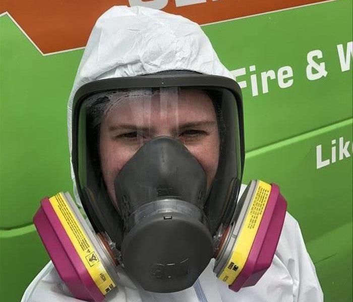 A SERVPRO of Mandarin employee dressed in a full face respirator and coveralls standing in front of a SERVPRO van.