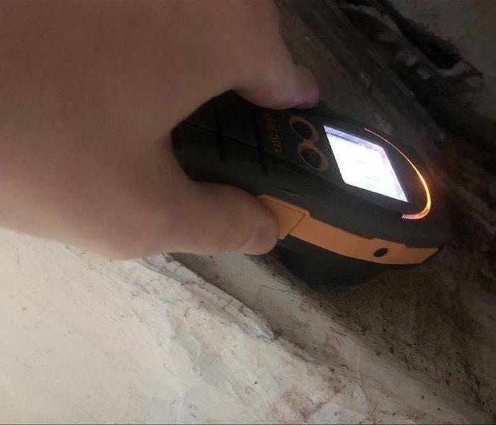 Photo shows a hand holding a grey and yellow moisture meter against moldy ductwork.